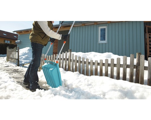 Une personne déblaie la neige avec une pelle à neige devant une maison.