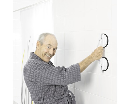 Un homme en peignoir fixe une barre d''appui avec des ventouses sur un mur carrelé.