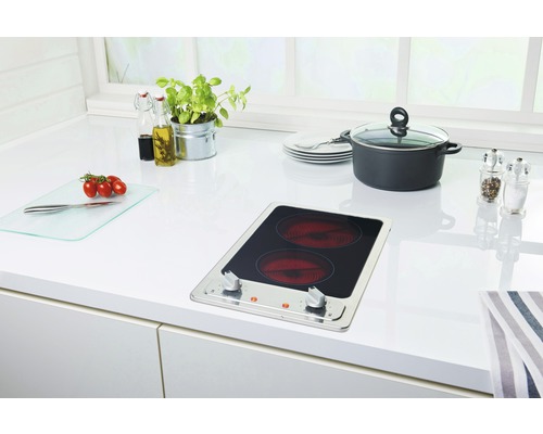 Scène de cuisine avec plaque de cuisson, casserole, vaisselle et aliments sur un plan de travail blanc.