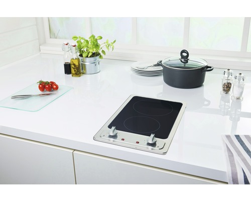 Scène de cuisine avec plaque de cuisson, casserole, planche à découper et ustensiles de cuisine sur un plan de travail blanc.