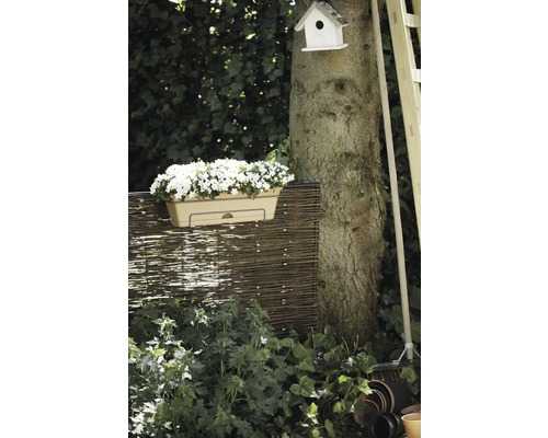 Gartenszene mit Blumenkasten, Flechtzaun, Baumstamm, Vogelhaus und Gartengeräten.