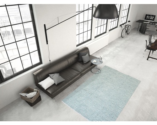 Helles Wohnzimmer mit Sofa, Teppich mit geometrischem Muster, Lampe und Fenstern