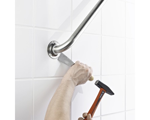 Une personne retire une barre d''appui du mur à l''aide d''un marteau et d''un burin.