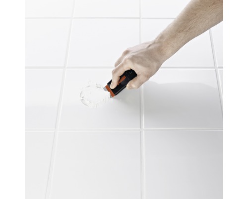 Main avec un grattoir à joints enlevant le mortier entre les carreaux.