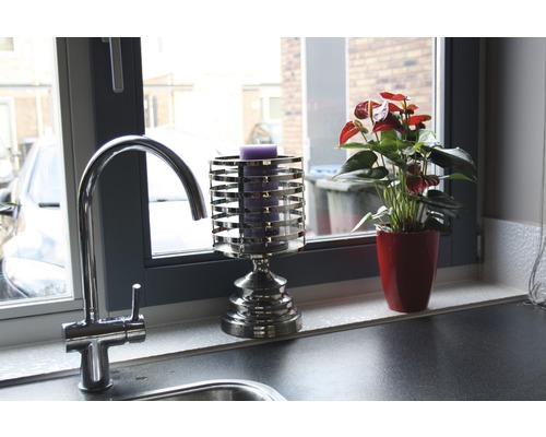 Dekoratives Stillleben mit Wasserhahn, Kerzenhalter und Zimmerpflanze auf einer Fensterbank