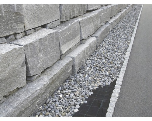 Un mur de soutènement en blocs de granit gris avec un lit de gravier.