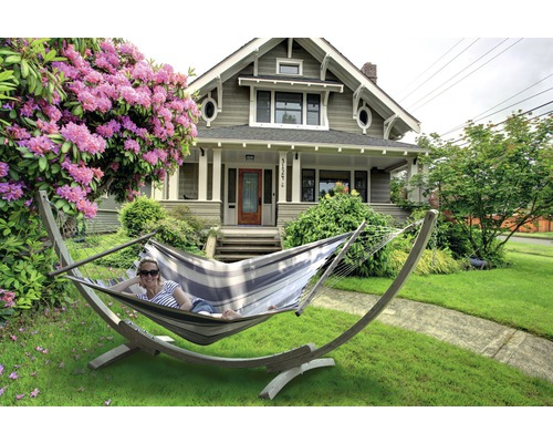 Frau entspannt in einer Hängematte im Garten vor einem Wohnhaus.