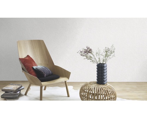 Salon avec fauteuil, coussins, table et décoration devant un mur blanc