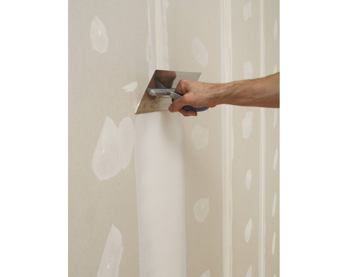 Ein Handwerker verspachtelt eine Gipskartonwand mit einem Spachtel.