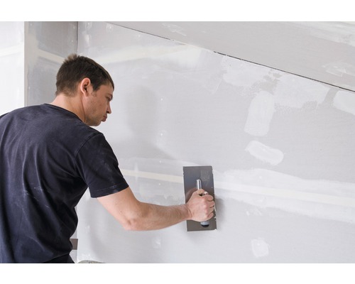 Ein Mann verspachtelt eine Gipskartonwand mit einem Spachtel