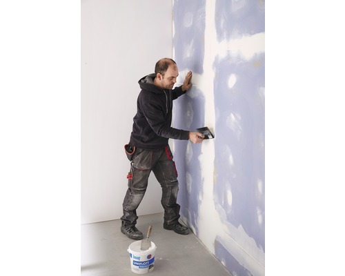 Mann spachtelt Wand mit Spachtelmasse und Spachtel