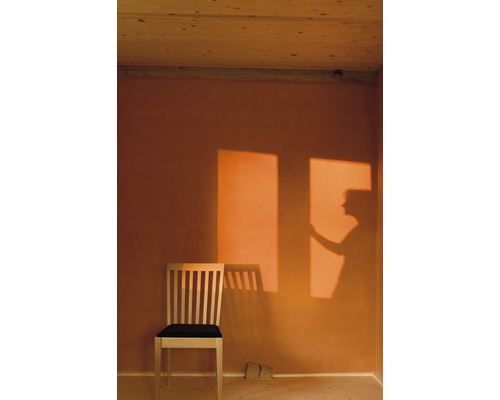 Innenraum mit Holzdecke, beiger Wand, Holzstuhl mit dunklem Sitzkissen und Schatten einer Person