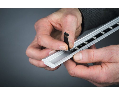 Une personne installe une bande LED dans un profilé en aluminium.