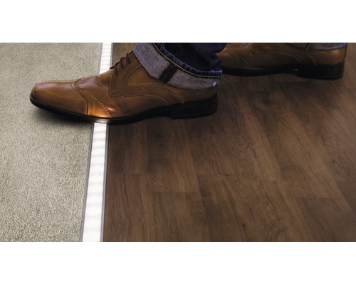 Personne passe du tapis au plancher en bois par un profilé LED