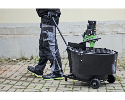 Une personne pousse une bétonnière sur roues sur des pavés.