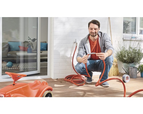 Un homme raccorde un tuyau d''arrosage à un robinet extérieur