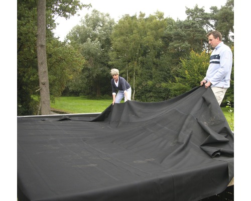 Deux personnes posent une bâche de bassin dans le jardin.