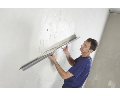 Homme lissant du plâtre sur un mur avec une taloche