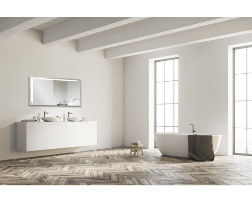 Helles Badezimmer mit Waschtisch, Spiegel mit Beleuchtung und Badewanne vor einem Fenster