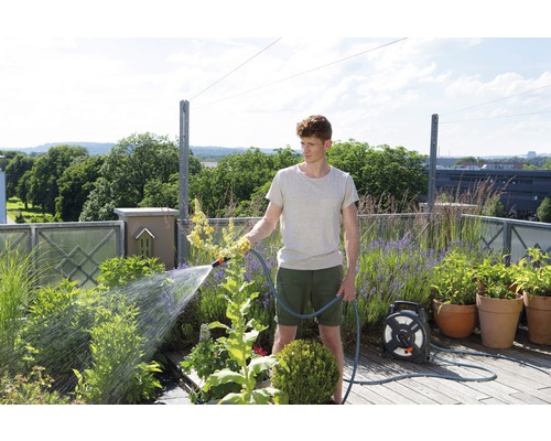 Mann gießt Pflanzen mit einem Gartenschlauch auf einer Dachterrasse