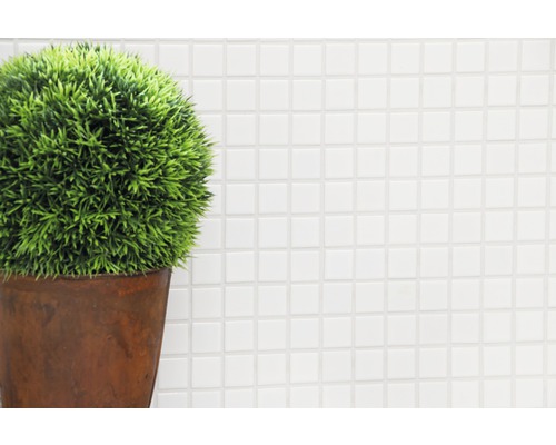 Plante artificielle décorative en pot devant un fond de mosaïque blanche