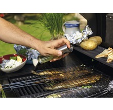 Eine Person besprüht Fisch auf einem Grill mit Öl.