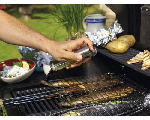 Eine Person besprüht Fisch auf einem Grill mit Öl.