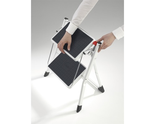 Eine Person klappt eine zweistufige Haushaltsleiter aus.