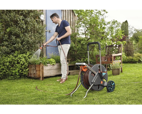 Mann bewässert Pflanzen mit einem Gartenschlauchwagen im Garten.