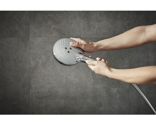 Une personne tient une pomme de douche devant un mur gris