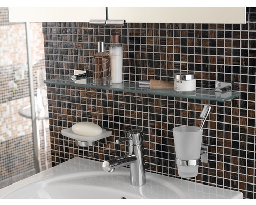 Lavabo de salle de bain avec robinet, porte-savon, gobelet à brosse à dents et étagère en verre avec divers articles de bain