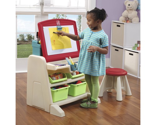 Kind malt auf einer Staffelei mit Aufbewahrungskörben und Hocker