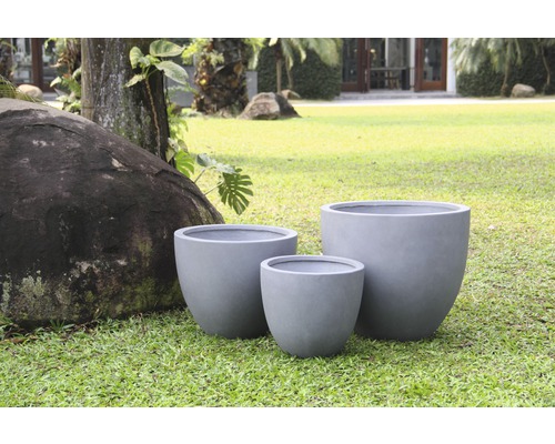 Drei graue Pflanzgefäße aus Faserzement auf einer Rasenfläche.