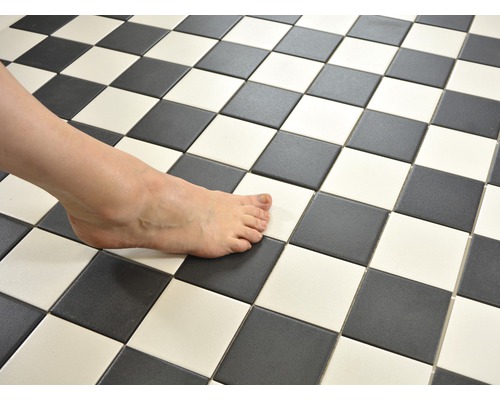 Schachbrettmuster aus schwarzen und weißen Fliesen mit nacktem Fuß