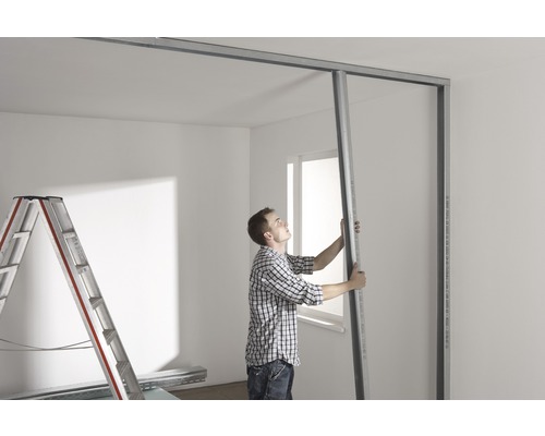 Mann montiert Trockenbauwand mit Metallprofilen in einem Raum.