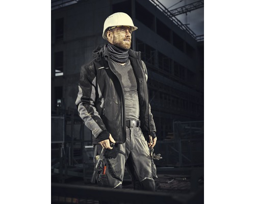 Un ouvrier du bâtiment avec un casque de protection porte des vêtements de travail devant un chantier.