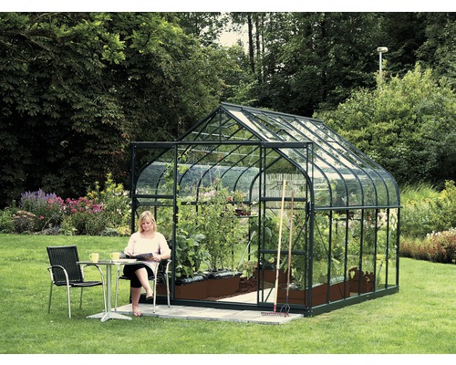 Gewächshaus Vitavia Diana 9900 Einscheibensicherheitsglas 3 mm 264x383 cm grün Gewächshaus mit Frau an einem Tisch im Garten.
