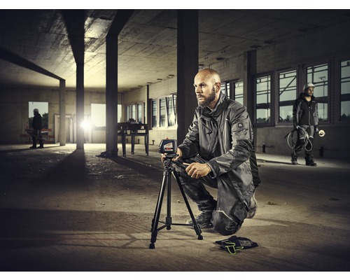 Un ouvrier est accroupi dans une coquille brute et utilise un niveau sur un trépied.