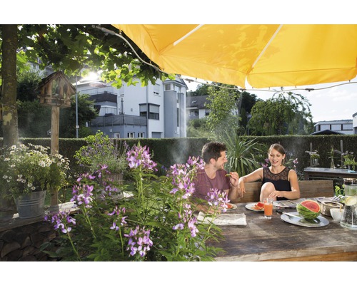 Paar sitzt an einem Holztisch im Garten unter einem Sonnenschirm und isst Wassermelone.