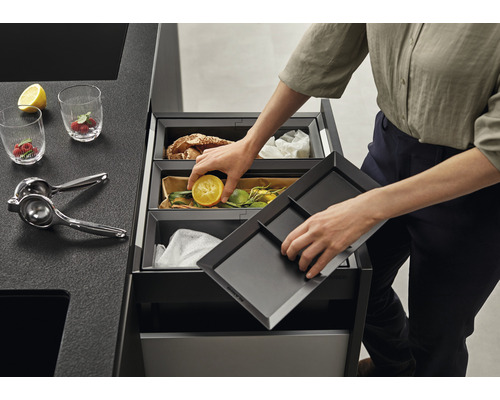 Système de tri des déchets avec trois bacs et une personne jetant un citron dans le bac du milieu.