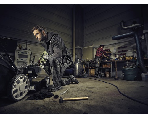 Atelier avec mécanicien réparant une tondeuse à gazon. À l''arrière-plan, une autre personne travaille sur un établi.