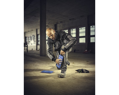Un homme fixe des genouillères à sa jambe sur un chantier
