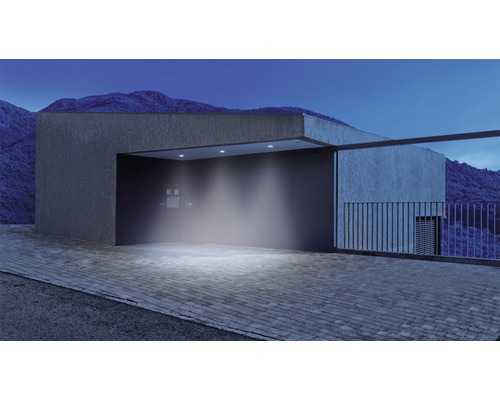 Beleuchtete Hofeinfahrt mit moderner Architektur und Berglandschaft im Hintergrund