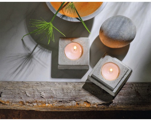 Mise en scène avec deux bougeoirs à réchaud en béton, une boule de pierre et une plante dans un bol