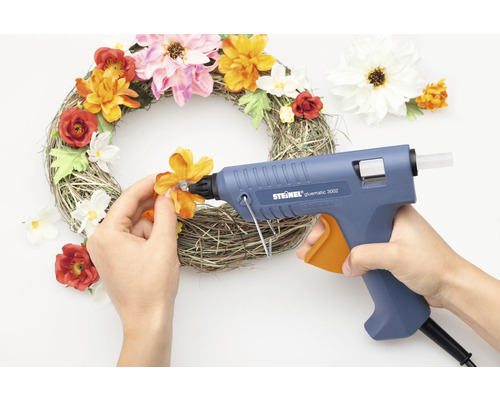 Une personne colle des fleurs sur une couronne à l''aide d''un pistolet à colle.