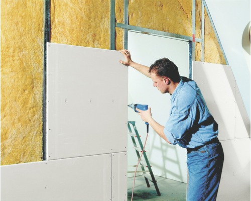 Un homme fixe une plaque de plâtre sur un mur avec isolation