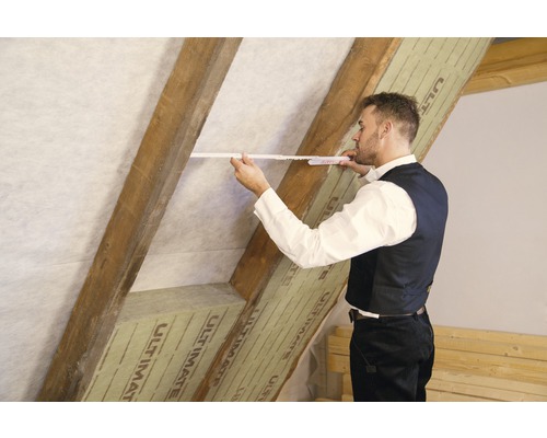 Un homme mesure la pente du toit avec un mètre pliant, les chevrons étant recouverts d''un matériau isolant.