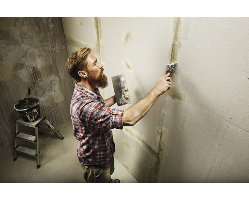 Un homme enduit un mur avec du mastic et des outils