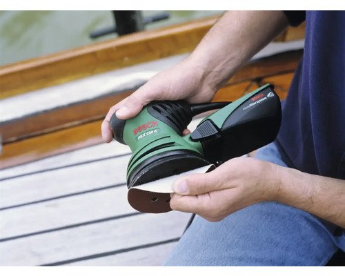 Eine Person befestigt Schleifpapier an einem Exzenterschleifer von Bosch PEX 220 A.