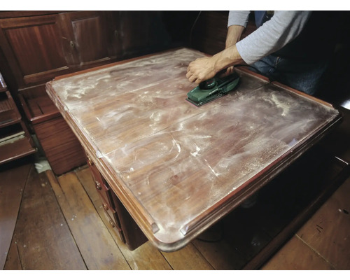 Eine Person schleift eine Holzoberfläche mit einem Elektroschleifer.